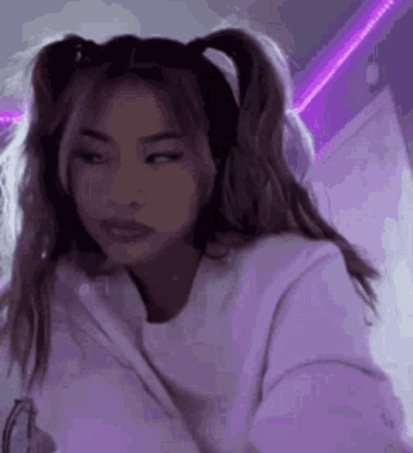 a girl with pigtails is wearing a white hoodie and a purple light behind her .
