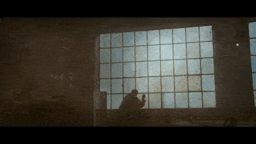 a man stands in front of a large window looking out