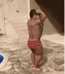 a shirtless man in red and white striped swim trunks is standing in a pool .