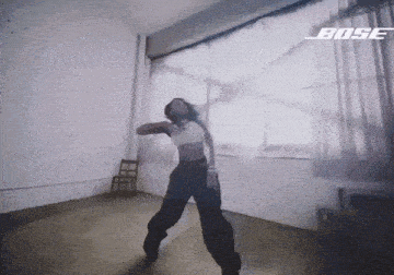 a woman is dancing in a room with a bose logo on the bottom of the screen .