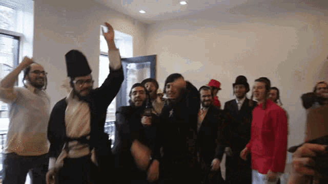 a group of people are dancing in a room and one man is wearing a hat