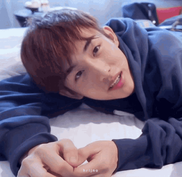 a young man in a blue hoodie is laying on a bed with his hands folded