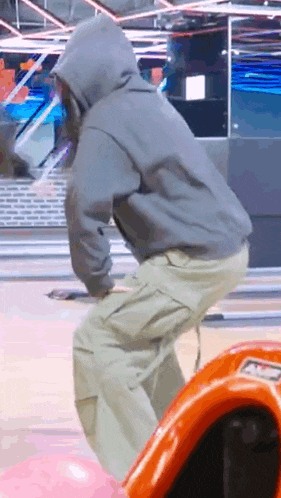 a man in a hoodie is riding a bowling alley ball .