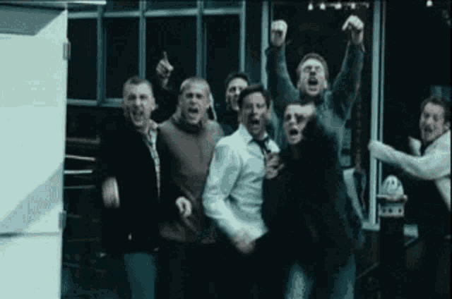 a group of men are standing in front of a building with their arms in the air