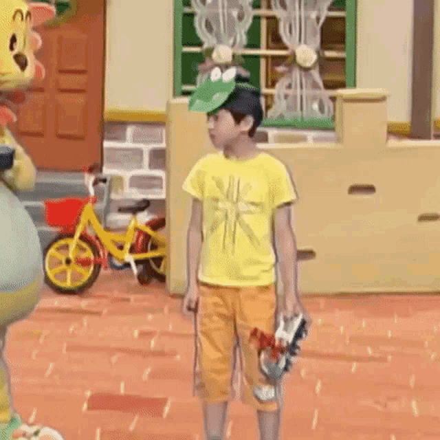 a young boy wearing a yellow shirt and orange shorts is standing in front of a yellow bicycle .