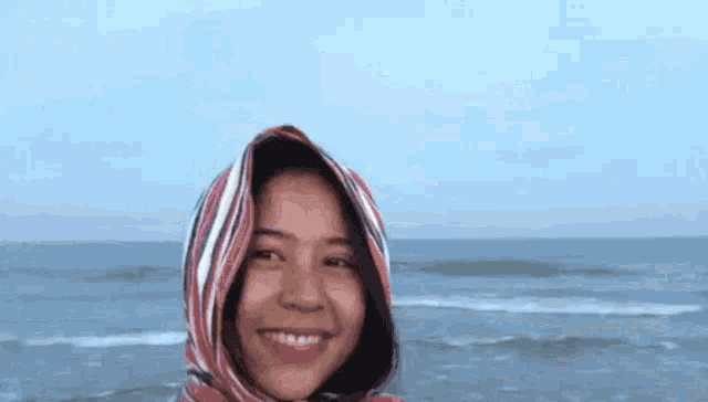 a young woman wearing a scarf around her head is smiling on the beach .