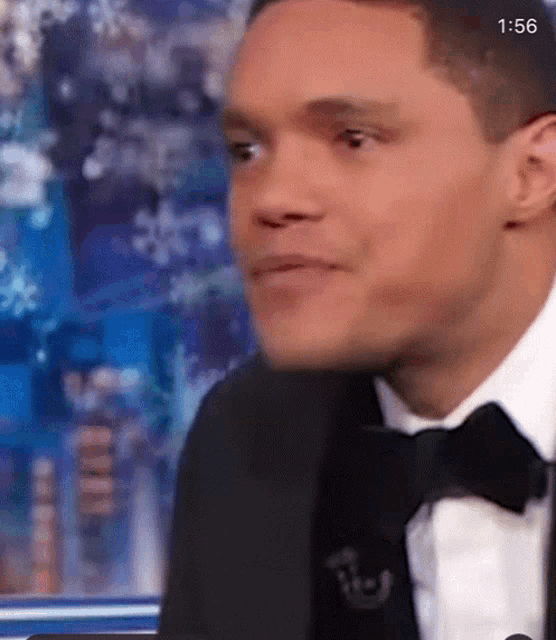 a man in a tuxedo and tie is sitting in front of a microphone .