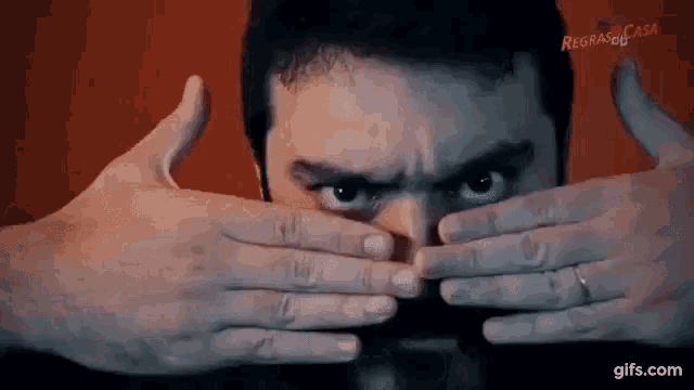 a man is covering his face with his hands and looking at the camera .