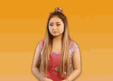 a woman with long hair is covering her face with her hand while wearing a pink apron .