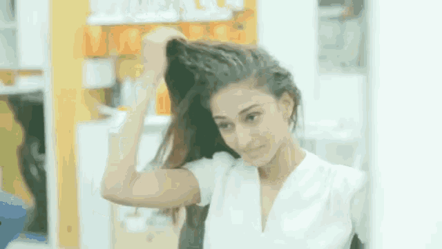 a woman in a white shirt is touching her hair in front of a mirror .