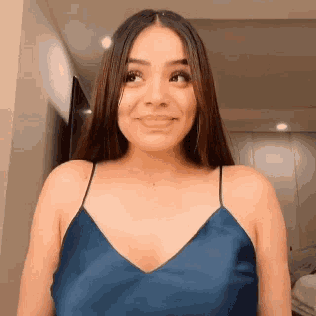 a woman wearing a blue tank top is smiling and looking at the camera