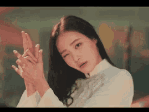 a woman in a white dress is holding her hands together and making a peace sign .