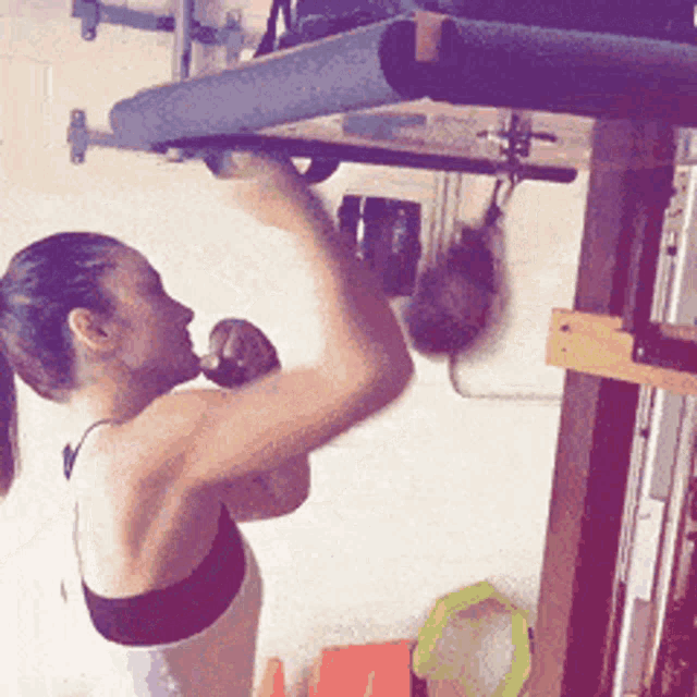 a woman is doing a pull up on a bar in a gym