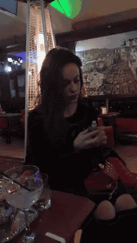 a woman sitting at a table with a martini glass in front of a painting