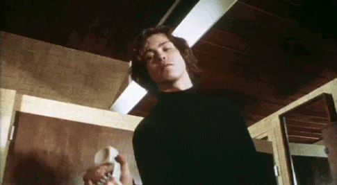 a man in a black sweater is standing in a room holding a telephone .