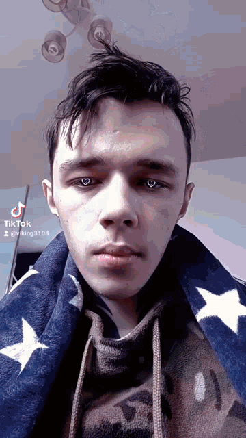 a young man wearing a hoodie and a blanket with stars on it looks at the camera .