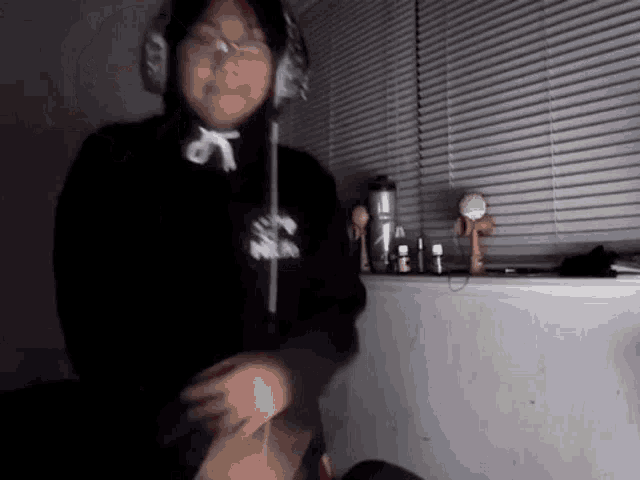 a person wearing headphones and a black hoodie is standing in front of a window in a dark room .