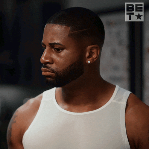 a man with a beard wearing a white tank top and earrings