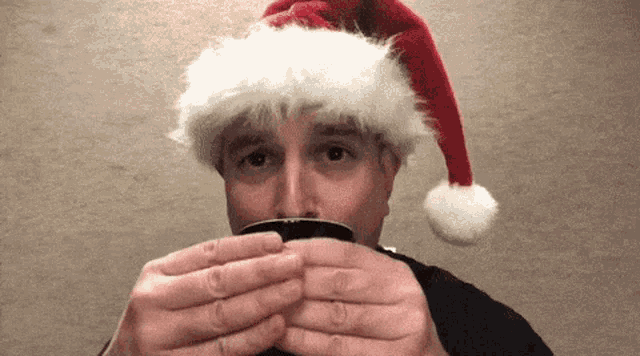 a man wearing a santa hat holds a cup of coffee