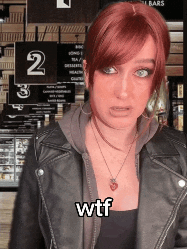 a woman with red hair is wearing a leather jacket and a necklace with the word wtf written on it