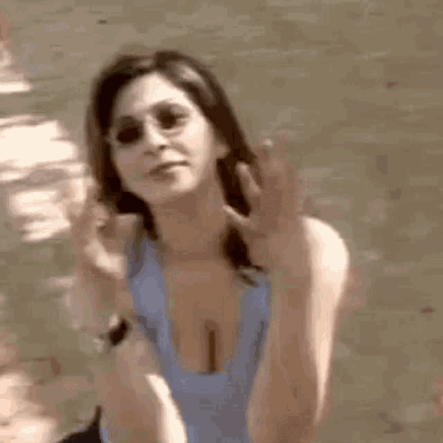 a woman wearing sunglasses and a blue tank top is waving her hand .