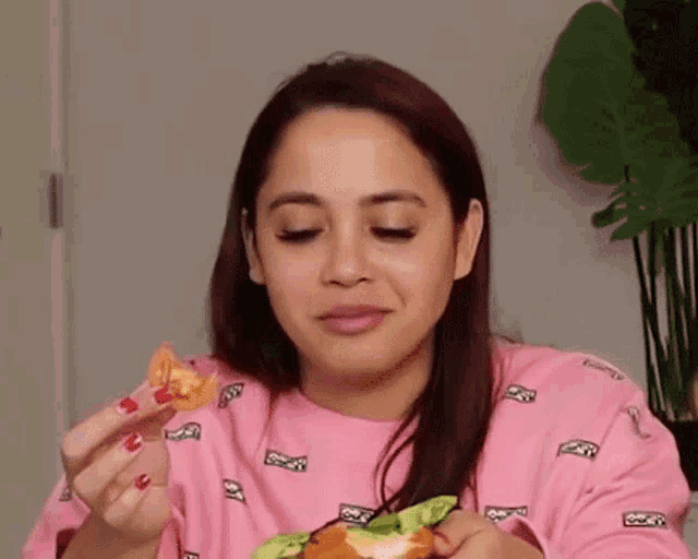 a woman in a pink shirt is eating a hamburger while holding a piece of food .