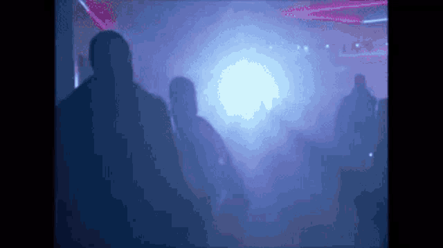 a group of people are standing in a dark room with purple lights and smoke .