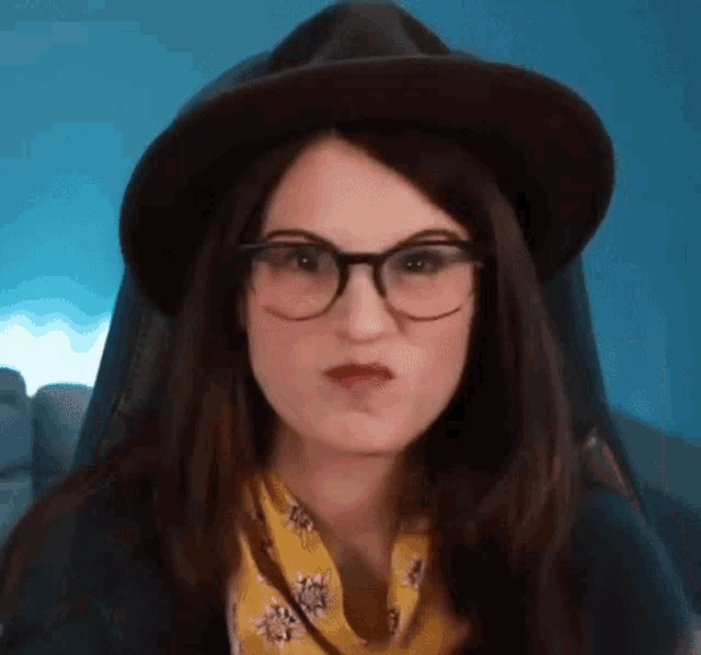 a woman wearing glasses and a hat is making a face .