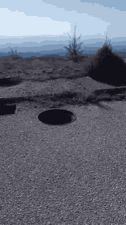 a hole in the ground in the middle of a gravel field