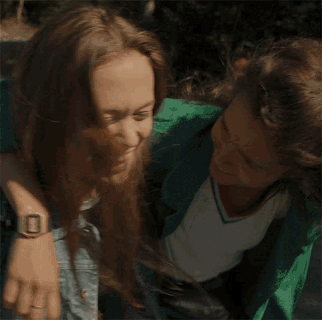 a woman in a green jacket is covering another woman 's eyes