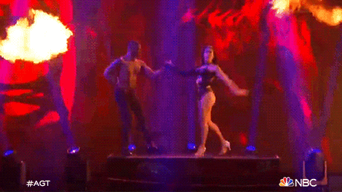 a man and a woman are dancing on a stage with flames in the background and a nbc logo in the corner