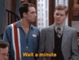 two men in suits are standing next to each other and one of them is telling the other to wait a minute .