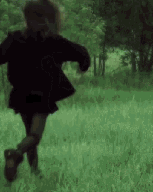 a person in a black jacket and skirt is running through a grassy field .