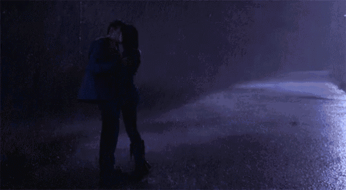 a man and a woman kissing in the rain at night .