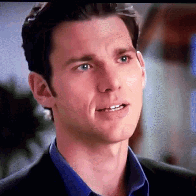 a close up of a man 's face with a blue shirt and a suit .