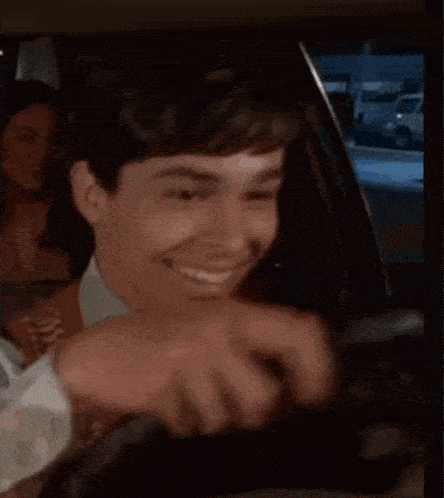 a man is driving a car and smiling while holding the steering wheel