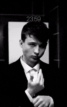 a young man in a suit looks at himself in a mirror with the time 23:59