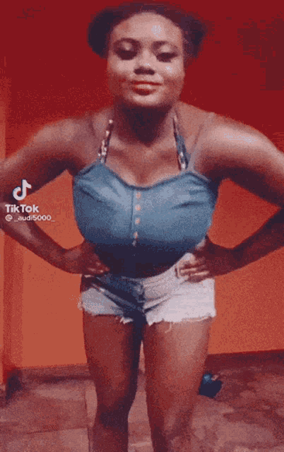 a woman in a blue top and white shorts is dancing in front of a red wall