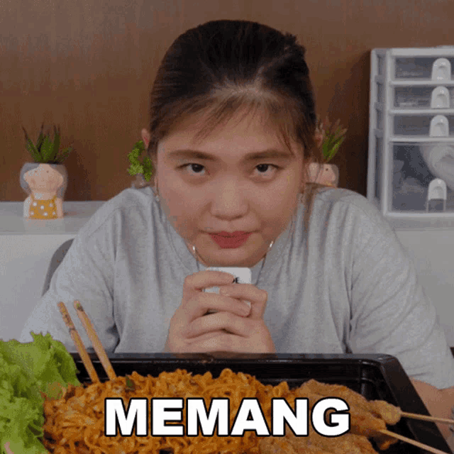 a woman eating noodles with the word memang on the bottom right