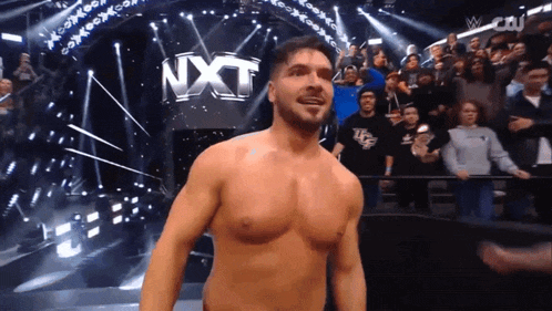 a shirtless wrestler is standing in front of a nxt sign