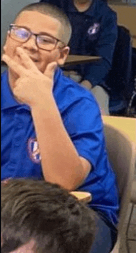 a young boy wearing glasses and a blue shirt is sitting at a table in a classroom .