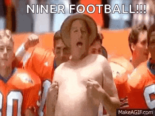 a shirtless man wearing a cowboy hat is standing in front of a crowd of football players .