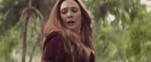 a close up of a woman 's face with red hair standing in a forest .