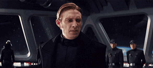 a man with red hair is standing in front of a group of men in black uniforms
