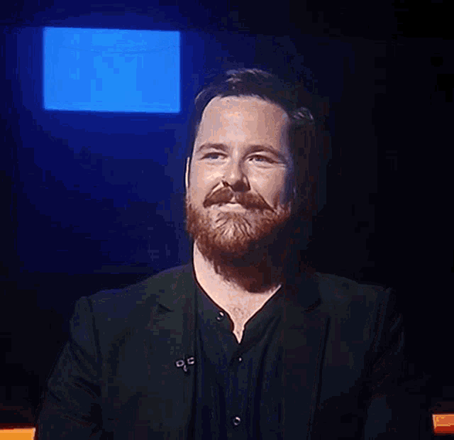 a man with a beard is smiling in front of a blue light