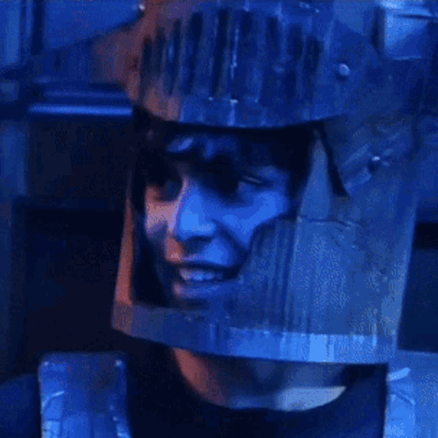 a man wearing a cardboard knight 's helmet looks at the camera with his eyes closed