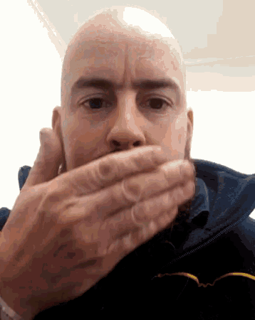a bald man with a beard is covering his mouth with his hand