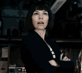 a woman with short hair and a black jacket is standing with her arms crossed