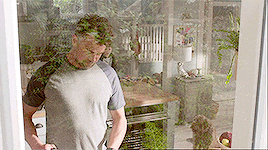 a man in a gray shirt is standing in front of a glass door in a kitchen .