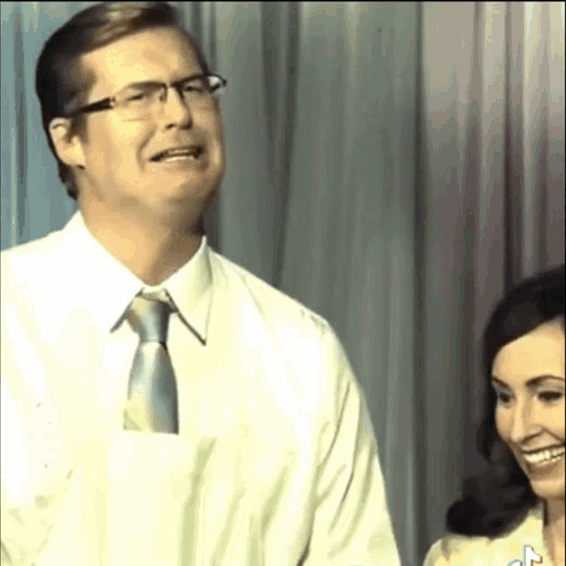 a man wearing glasses and a tie is standing next to a woman
